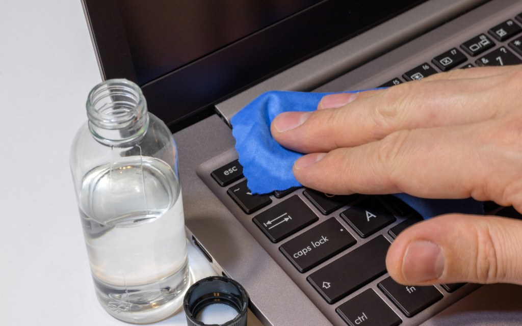 Wiping laptop keyboard with microfiber cloth and cleaning solution